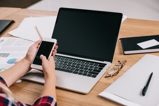A cropped picture of a woman using her computer and smartphone 