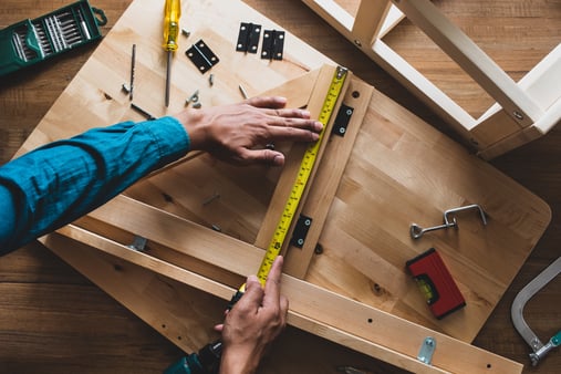 Hands measuring a piece of wood on a work bench. 