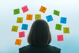 back view of woman looking at question marks on wall with white background