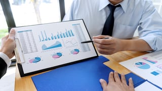 Person pointing to graphs on a screen with a pen.