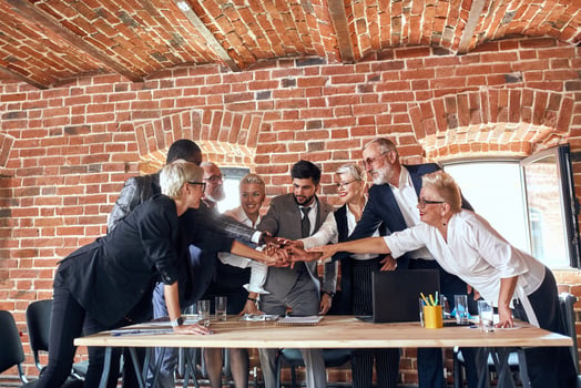 Group of diverse business people joining hands together in boardroom.