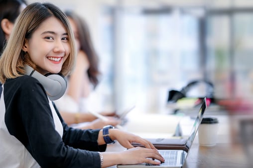 Portrait of young woman smiling and looking at camera while working in modern office with her friends.