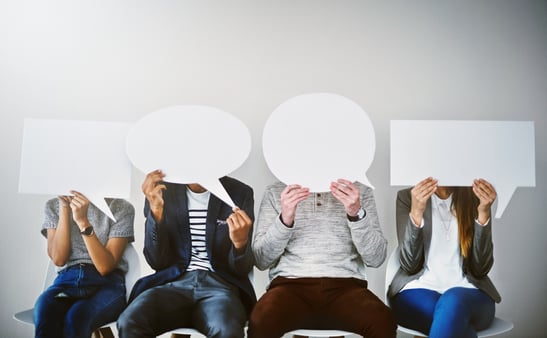 Four business people with cardboard speech bubbles in front of their faces 