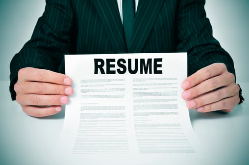 Person holding up a piece of paper that says resume