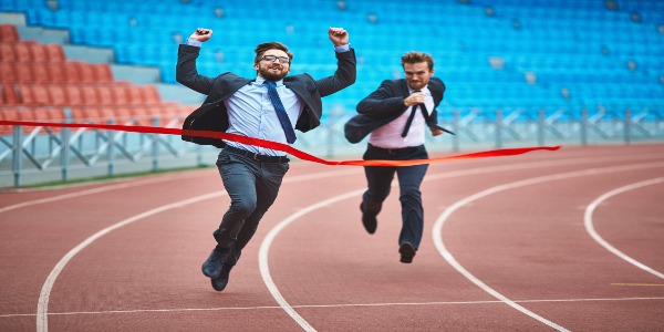 Two men in suits racing on a track. One is about to cross the finish line. 