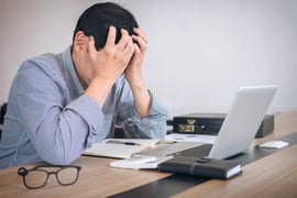 Furstrated businessman sitting at his computer with head in his hand 
