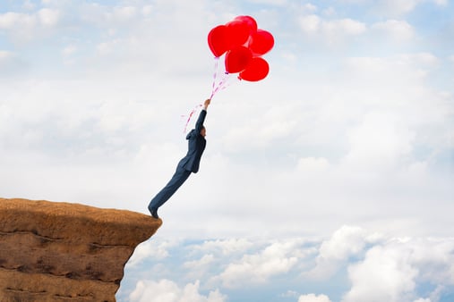 Businessman flying with red balloons on the edge of a cliff.
