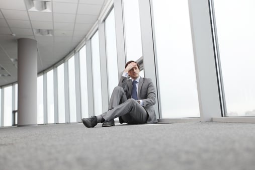 Businessperson sitting on the floor of a gray, boring office environment
