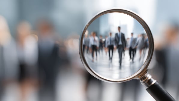 The concept of recognizing something in your business. Someone holding a magnifying glass up to business people. 