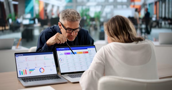 A sales leader points to a CRM pipeline board on a laptop while reviewing open opportunities with a colleague across the table.
