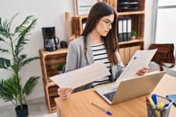 Woman in a gray blazer comparing two benefits documents at her desk during open enrollment.