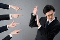 Four hands with accusing fingers pointing at a businessperson. 
