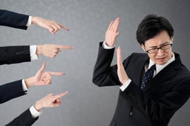 Four hands with accusing fingers pointing at a businessperson. 