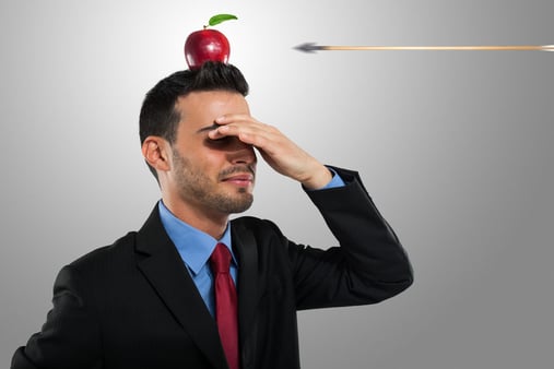 A man with his hand over his eyes and balancing an apple on his head 