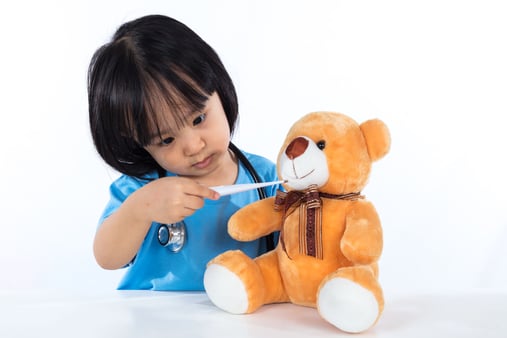 A little girl taking her teddy bear's temperature
