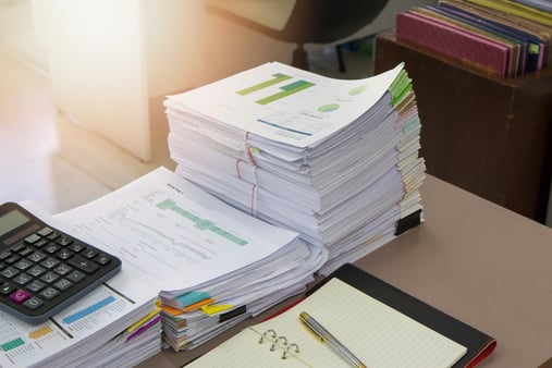 A pile of paper documents on a desk along with a notepad and calculator