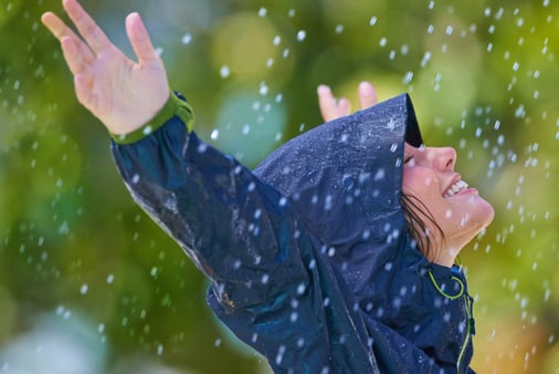 A woman in a blue raincoat enjoying herself outside in the rain 