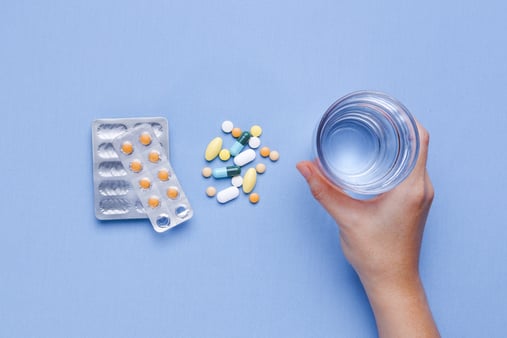 A hand holding a glass of water and medication to the left of the hand