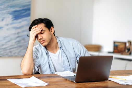 A man who is sitting at his desk with his hand on his forehead