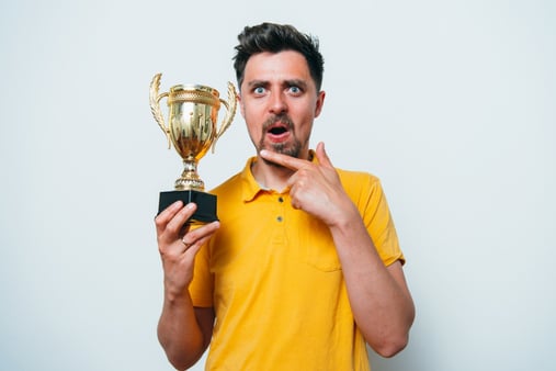 Concept of being the best. A man excitedly holding and pointing at a trophy. 