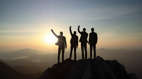 Four businesspeople in silhouette standing on top of a mountain
