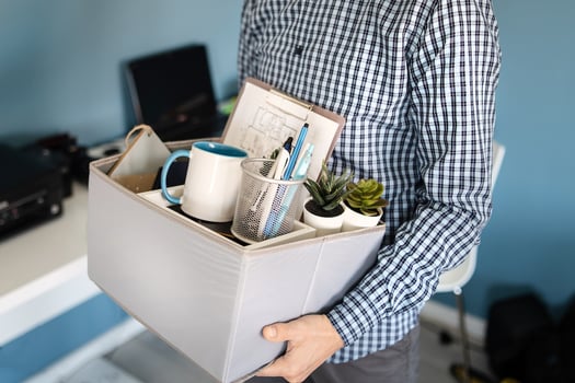 Guy holding a box with personal items leaving the office after being fired 