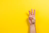 A hand holding up three fingers on a yellow background 