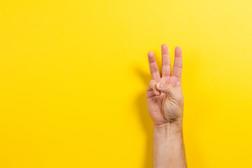 A hand holding up three fingers on a yellow background 