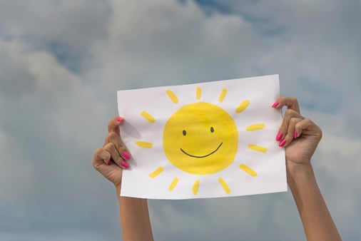 A pair of hands holding up a piece of paper with a sun on it 