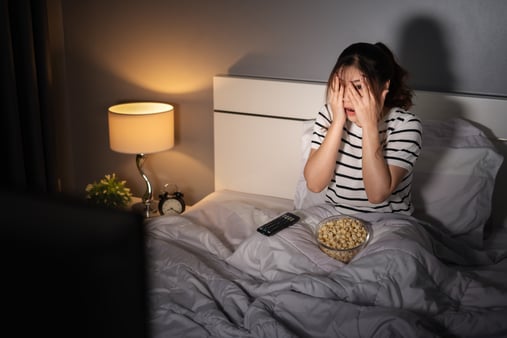 Woman sitting on bed and covering her face with her hands