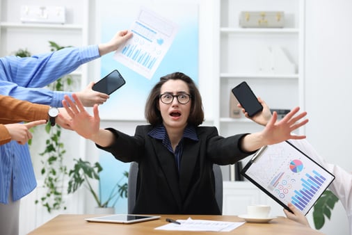 Woman overwhelmed by different requests from colleagues at desk in office