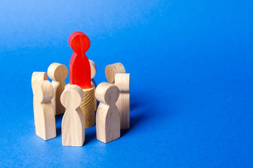 Concept of marketing messaging and standing out in a crowd of competitors. A red pawn piece above a group of wooden pawn pieces. 