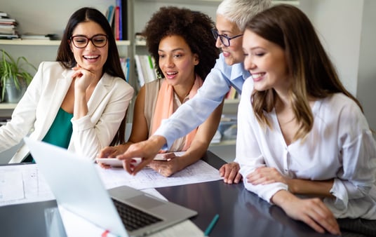 Four women leaders gather around a laptop, sharing ideas and laughter as they collaborate on a creative project. Their diverse backgrounds enrich the brainstorming session.
