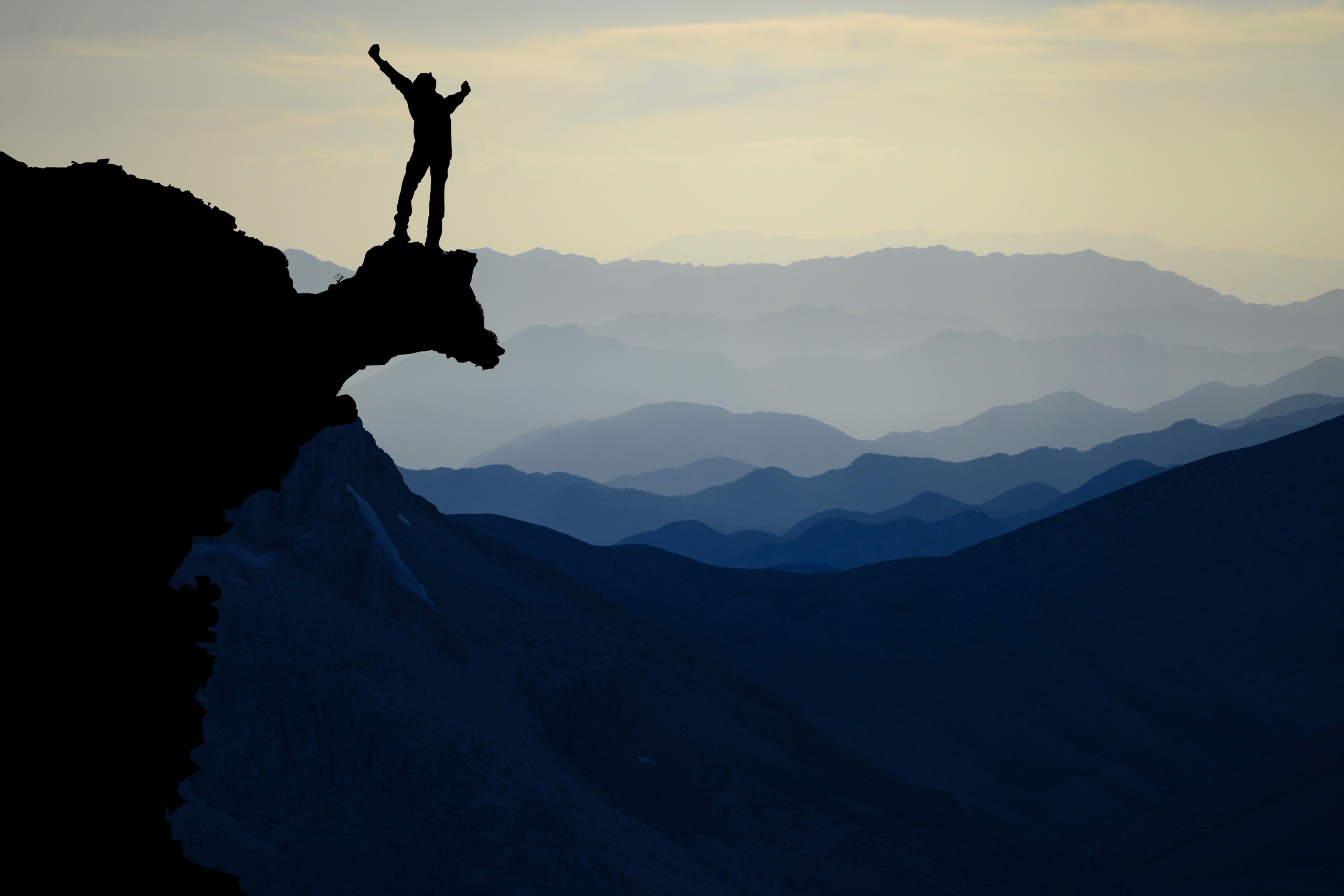 person standing in a victory pose on top of a mountain 